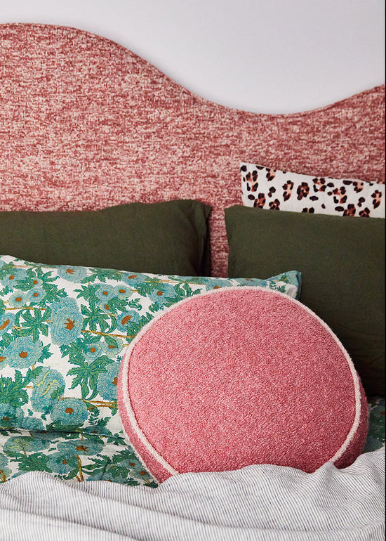 Bed with pink headboard, green and floral-patterned pillows, and a pink round pillow.
