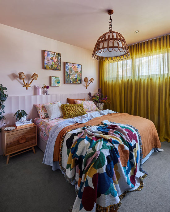 After: Barwon Heads bedroom designed by Nikki McGar Interiors featuring colourful artwork, layered bedding, and indoor plants against a calm, neutral backdrop.