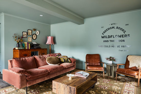 After: Bright Airbnb living room designed by Nikki McGar Interiors featuring green walls, custom wall art, pink velvet sofa by House of Orange, vintage treasures and comfy leather chairs for a relaxed feel.