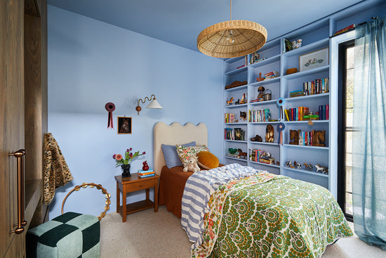 After: Kid’s bedroom designed by Nikki McGar Interiors featuring blue walls, a custom-built blue wall to wall bookshelf, and layered bedding for a playful yet timeless look.