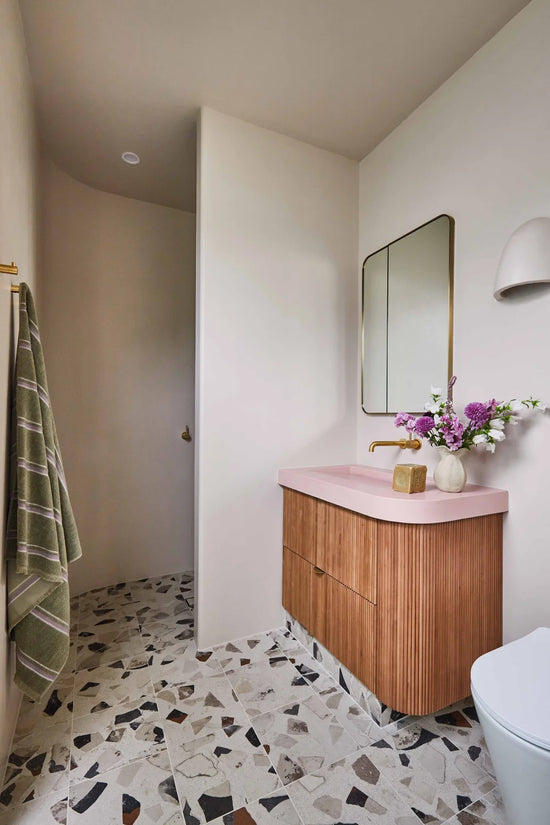 Barwon Heads bathroom renovation by Nikki McGar Interiors with terrazzo, microcement, and pink concrete basin accented by brass tapware.
